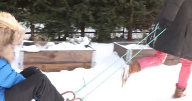 Anne oğlunu kızağa çekiyor, anne oğlunu kızakta otururken çekiyor.