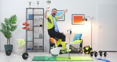 Profesyonel bisikletçi, yarışı kazanıp kupayı tuttuktan sonra zaferle ellerini kaldırdı. Bisikletli sporcu evde zaferi kutluyor. Spor komedisi, komik sporcu