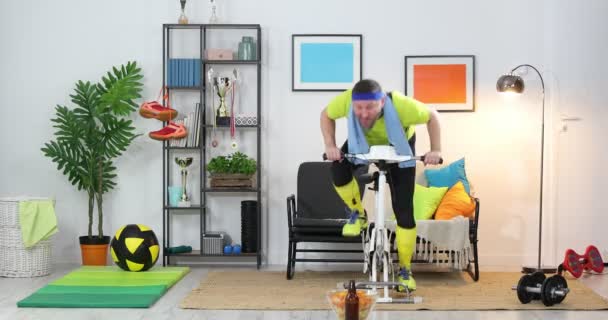 Hombre Joven Atleta Una Bicicleta Estacionaria Está Haciendo Ejercicio Casa — Vídeos de Stock