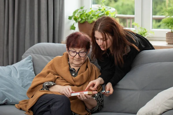 一个快乐的年轻女人帮一位老年妇女开药方 青少年向年长女性展示如何使用每周一次的不同类型的药丸组织者 图库图片