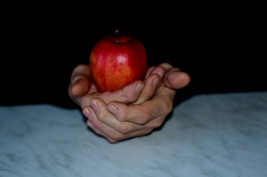 Yaşlı adamın elleri bir elma tutuyor.
