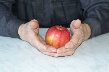 Yaşlı adamın elleri bir elma tutuyor.