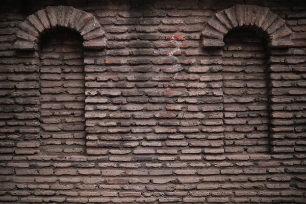 Dark brick factory wall with two rounded sealed windows