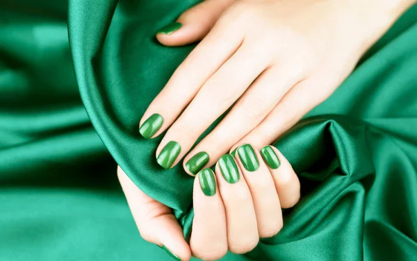 Female hands with bright green manicure on a silk green background. Close up