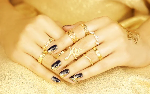 Female hands with black and gold manicure on a gold background. Close up.