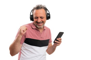 Yetişkin adam modeli kulaklıkla müzik dinlemekten zevk alıyor. Elinde akıllı telefon, beyaz arka planda izole edilmiş telif alanı eşliğinde dans ediyor.