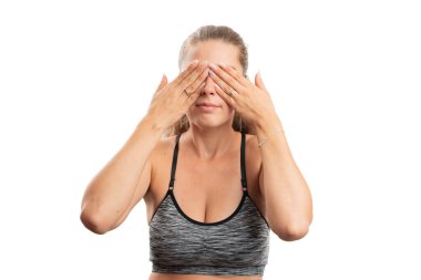 Yetişkin model kadın spor kıyafetleri giyiyor gözleri örtüyor elleri gizli bir konsept olarak kullanıyor aktif yaşam tarzı beyaz stüdyo arka planında izole edilmiş.