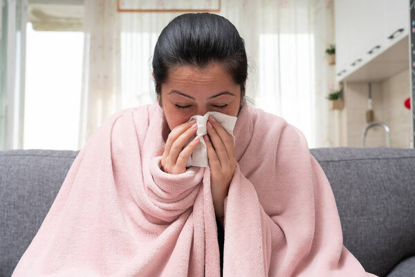 Sick adult female model on sofa blowing stuffy nose as sinusitis concept having sars covid flu influenza symptoms