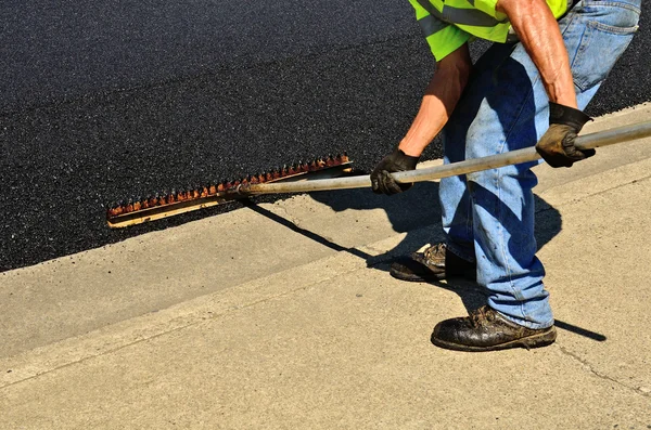 Trabajador usando un rastrillo para empujar el exceso de asfalto — Foto de Stock