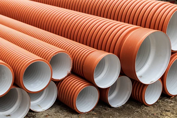 Yeni turuncu plastik kanalizasyon boruları dışarıda bulunuyor. Farklı çaplarda boruları olan bir inşaat alanı. Soyut Parça.