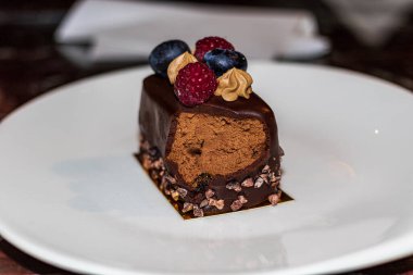 Beyaz tabakta bir dilim lezzetli pasta. Pasta taze böğürtlen ve siyah çikolatayla süslenmiş. Yakın plan..