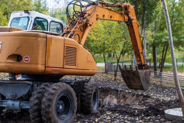 İnşaat alanındaki toprak işlerinde kazıcı yükleyici. Bir kazıcı yeni park alanı inşaatı için arazi kazıyor.