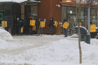 Kyiv Ukrayna - 11 Şubat 2021: Reklam kutularıyla teslimat görevlileri yoğun bir kar yağışı sırasında bir fast food restoranının önünde siparişleri bekliyorlar. Şiddetli kar fırtınası.
