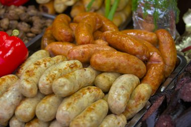 Kırmızı dolmalık biber ve diğer ürünlerin yanında büyük bir tepside çeşitli türde et sosisleri bulunur. Açık ateşte pişirilen lezzetli yemekler, sokak yemekleri fuarında sunuluyor..