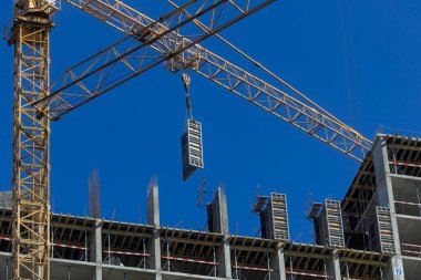 Yeni binanın en üst katında inşaat halindeki büyük yapılar vinç kullanılarak inşa ediliyor. Modern apartmanlar ve yeni bir konut kompleksi inşaatı. Mavi gökyüzü.