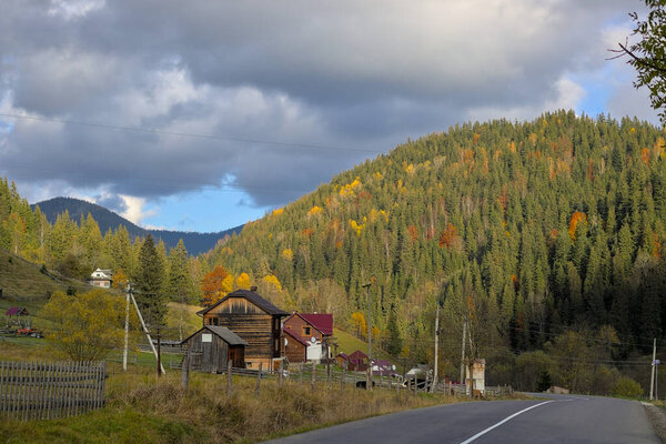 A small village located on steep mountain slopes. Autumn mountain landscape in the Ukrainian Carpathians - yellow and red trees combined with green needles.