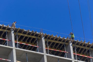 Kyiv, Ukrayna - 31 Ağustos 2021: Profesyonel yüksek binalar yapım aşamasındaki bir binanın en üst katında çalışıyor. Modern evler ve konut kompleksi inşaatı. Mavi gökyüzü.