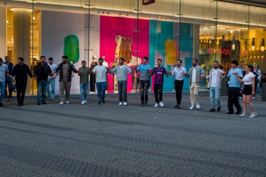 Nuremberg, Almanya - 23 Ağustos 2025: Parlak cam yapının yanında dans eden canlı bir kalabalık, Almanya 'nın Nurnberg kentinde el ele tutuşuyor. Kahkaha ve ritim uyum içinde hareket ettikçe havayı doldurur..