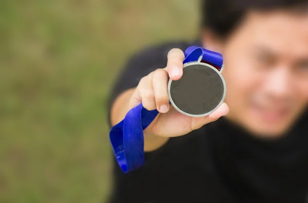 Ángulo ascendente de atleta asiático sosteniendo medalla de oro genérica con cinta en la mano . —  Fotos de Stock