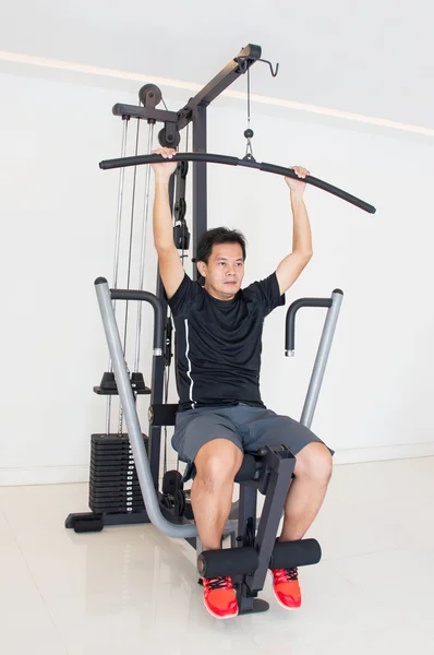 Azjatycki człowiek robi ćwiczenia na maszynie Fitness w siłowni. — Zdjęcie stockowe