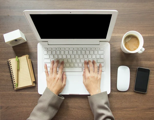 Uma mulher está trabalhando usando um computador portátil na mesa de madeira. Mãos a datilografar num teclado. Vista superior . — Fotografia de Stock