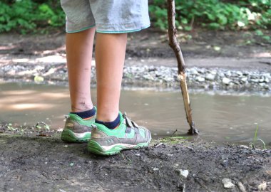 Kirli ve sivrisinekler, çamurlu su birikintisinin yanında duran beyaz çocuğun bacaklarını ısırdı. Ellerinde bir sırık, kirli sudaki çamuru keşfediyor, doğanın dışında oynuyor..