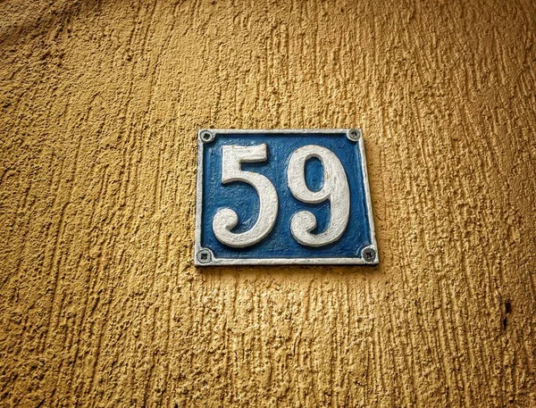 Number 59, the number of houses, apartments, streets. The white number on a blue metal plate, house number fifty-nine (59) on a rough wall.