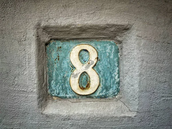 Number 8, the number of houses, apartments, streets. The white number on a blue metal plate, house number eight (8) on a rough wall.