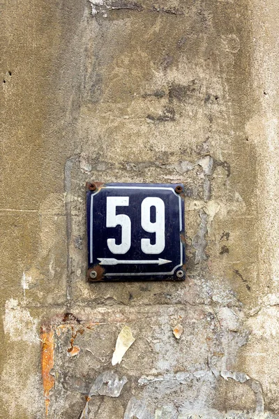 Number 59, the number of houses, apartments, streets. The white number on a blue metal plate, house number fifty-nine (59) on a rough yellow wall.