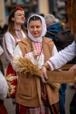 Kyustendil, Bulgaristan 07 Şubat 2026: Djamala Maskeli Balosu. Koyun postu giymiş ve yüzü boyalı bir kadın. Arkasında, ahşap boynuzlu bir maske vardı. Kötü ruhları defetmek için yapılan geleneksel ayinin bir parçasıydı..