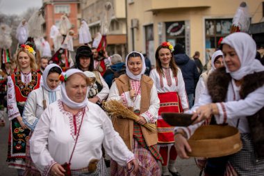 Kyustendil, Bulgaristan 07 Şubat 2026: Djamala Maskeli Balosu. Koyun postu giymiş ve yüzü boyalı bir kadın. Arkasında, ahşap boynuzlu bir maske vardı. Kötü ruhları defetmek için yapılan geleneksel ayinin bir parçasıydı..