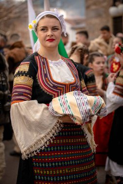 Kyustendil, Bulgaristan 07 Şubat 2026: Djamala Maskeli Balosu. Koyun postu giymiş ve yüzü boyalı bir kadın. Arkasında, ahşap boynuzlu bir maske vardı. Kötü ruhları defetmek için yapılan geleneksel ayinin bir parçasıydı..