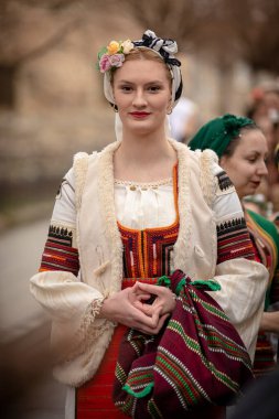 Kyustendil, Bulgaristan 07 Şubat 2026: Djamala Maskeli Balosu. Koyun postu giymiş ve yüzü boyalı bir kadın. Arkasında, ahşap boynuzlu bir maske vardı. Kötü ruhları defetmek için yapılan geleneksel ayinin bir parçasıydı..