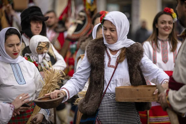 Kyustendil, Bulgaristan 07 Şubat 2026: Djamala Maskeli Balosu. Koyun postu giymiş ve yüzü boyalı bir kadın. Arkasında, ahşap boynuzlu bir maske vardı. Kötü ruhları defetmek için yapılan geleneksel ayinin bir parçasıydı..