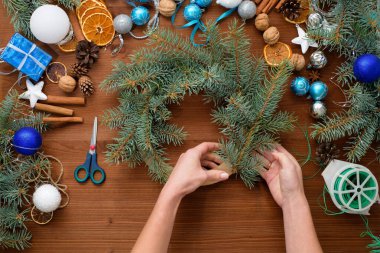 2021 boğasının gümüş ve mavi renklerinde ladin dalları, portakallar ve Noel toplarından evde adım adım bir Noel ağacı çelengi yapma süreci. tahta arkaplan üst görünümü.