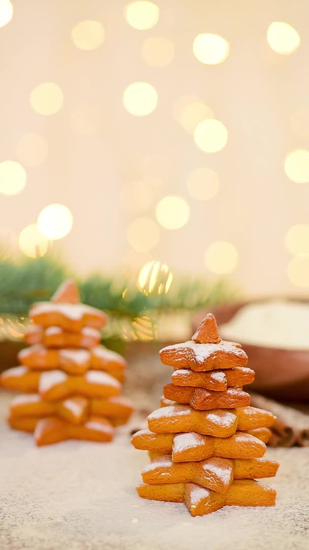 Pan de jengibre de Navidad en forma de árbol de Navidad y una estrella se espolvorea con azúcar en polvo contra la luz de guirnaldas bokeh. enfoque suave en la zanahoria, video vertical — Vídeo de stock