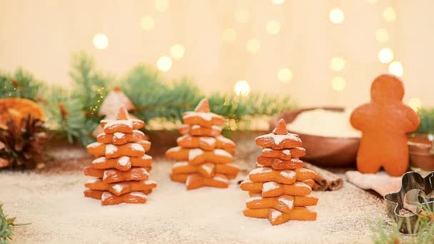 Lebkuchen in Form eines Weihnachtsbaums und eines Sterns werden mit Puderzucker gegen das Licht von Bokeh-Girlanden gestreut. weicher Fokus auf Lebkuchen, Zuckerschwaden. — Stockvideo