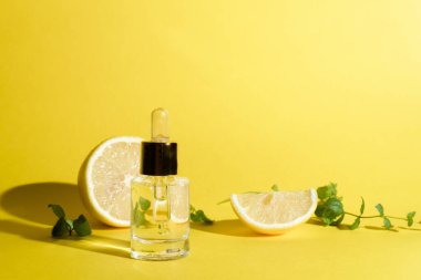 Yüz serumu, limonlu turunçgil ve cam şişede C vitamini, sarı arka planda pipet, evde cilt bakımı konsepti..