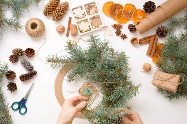 2021 'deki ladin dalları, portakallar ve ahşap çevre dostu oyuncaklardan noel ağacı çelengi yapma süreci. Beyaz arka plan manzarası. Ekolojik Noel kavramı, atıksız.