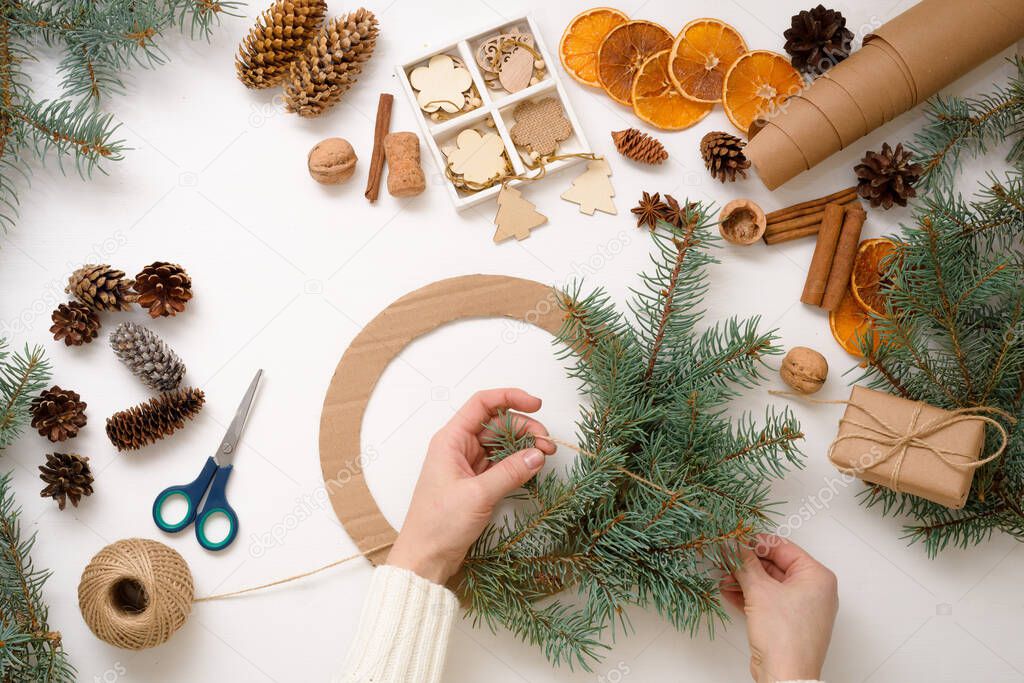 step-by-step process of making Christmas tree wreath at home from spruce branches, oranges and wooden eco-friendly toys in 2021. white background top view. concept of ecological Christmas, waste-free.