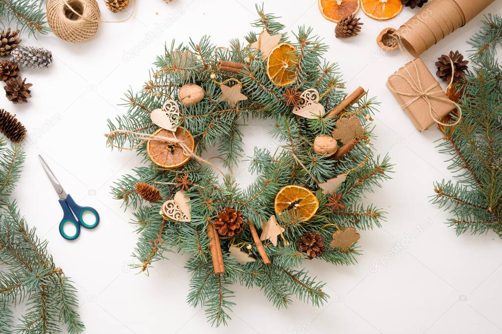 step-by-step process of making Christmas tree wreath at home from spruce branches, oranges and wooden eco-friendly toys in 2021. white background top view. concept of ecological Christmas, waste-free.