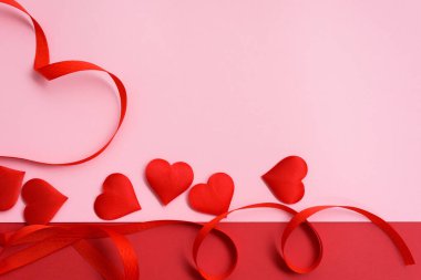 Sevgililer günü kırmızı kurdele pembe arka planda kalp şeklinde kıvrılır. düğün ve tebrik kartları için şenlikli arkaplan, maket, kopyalama alanı.