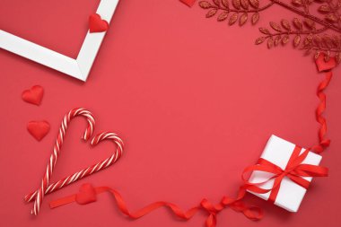 Kartpostalda mesaj için boşluk var. Sevgililer günü, kırmızı kurdeleli ve kalpli bir hediye, kırmızı arka planda kalp şeklinde lolipoplar. maketleme.