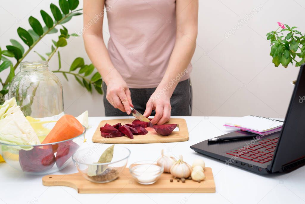 Cooking at home. woman watches online video recipes on a laptop and cooks in the kitchen at home, cutting vegetables. Pickled pink cabbage, fermented with beetroot and carrot in brine in a jar