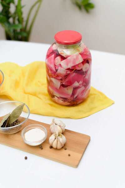 Маринованная розовая капуста ферментативная со свеклой и морковью в рассоле в банке на светлом фоне