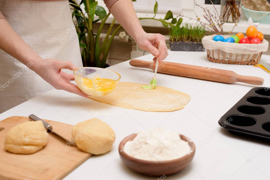 the process of rolling out the dough at home on the table is the hands of a woman for making cruffins festive pastries for Easter . side view of a bright kitchen , with painted eggs.