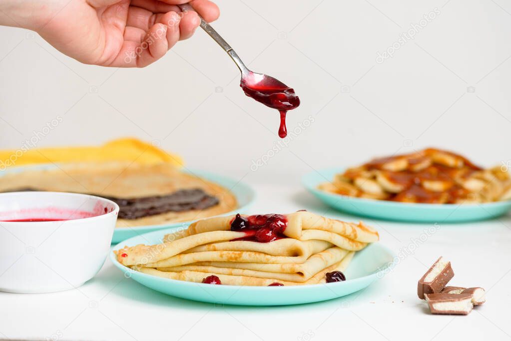 blini pancakes with red berry jam close-up on a blue plate on a light background . traditional Russian holiday is a symbol of spring and sweet dessert.