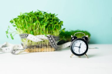 micro-green on the scale for measuring body weight, centimeter tape for the body, clock on a light background. means and items for a diet, a healthy lifestyle concept . vegan superfood trend. clipart