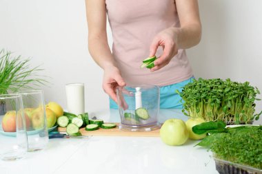 Adım adım mikro-yeşil elma salatalığı ve ıspanaktan meyve püresi yapma tarifi. Kadın elleri sebzeleri kesiyor ve onları miksere koyuyor. Hafif arka planda organik gıda detoksu için çırpıyorlar..