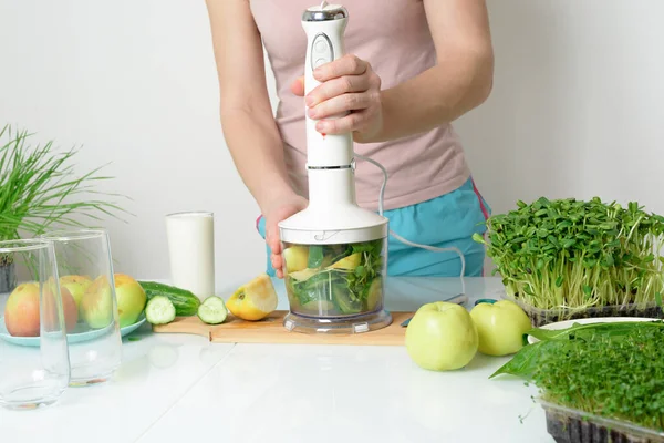step-by-step recipe for making smoothies from micro-green apples cucumber and spinach. woman hands cut vegetables and put them in blender for whipping eco organic fresh food detox on light background.